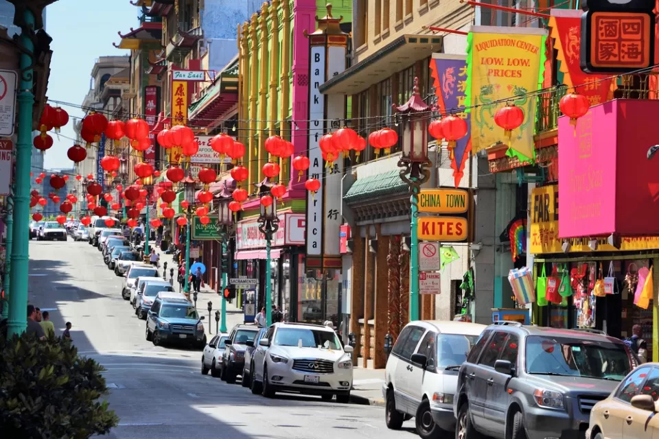 View of street in Chinatown, San Francisco with cars parked along curb and red Chinese lanterns hanging above street
